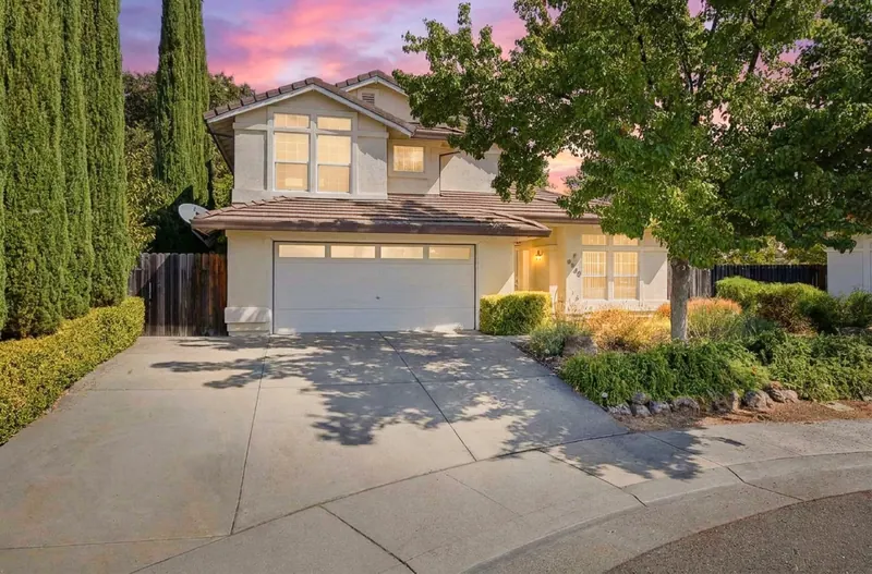 Two-story home framed by tall trees at sunset